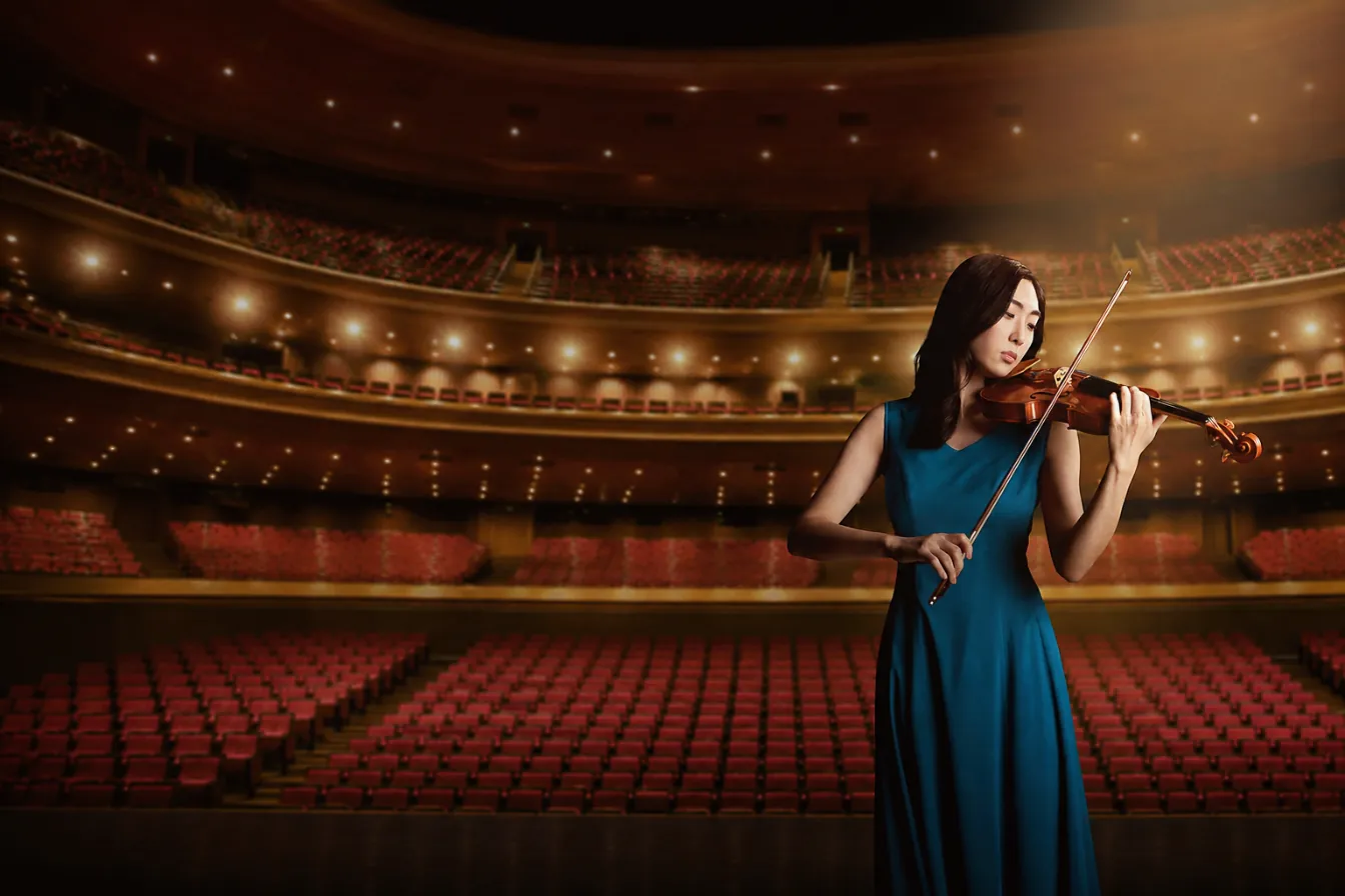 A violinist in a blue gown performing on an empty concert-hall stage